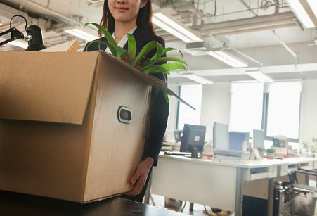 Une femme tenant une grande boîte en carton avec une plante verte à l'intérieur, dans un bureau mode.
